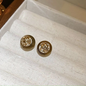 Detail of round tiger eye earrings with golden metal motifs in a white jewelry box
