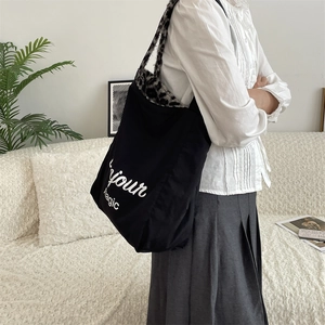 Detailed shot of black canvas tote bag featuring leopard print strap and Bonjour Magic text