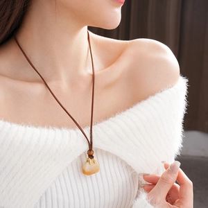 Macro detail of amber-style bag pendant with braided cord on white sweater