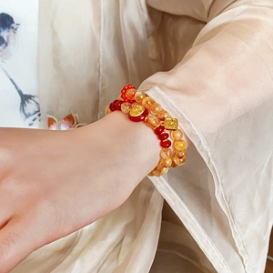 Detailed close-up of a double-layer red and gold beaded bracelet with a Fu pendant