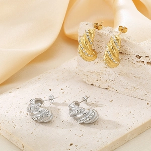Detail of twisted C-shape earrings in gold and silver with inlaid crystals on stone