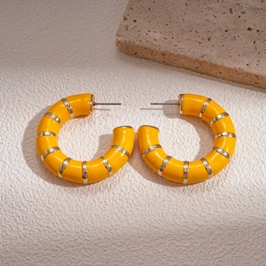 Macro view of large yellow enamel C-shaped hoop earrings with gold metal stripes
