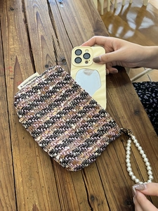Detail of pink tweed pouch featuring pearl handle and woven logo label on wooden table