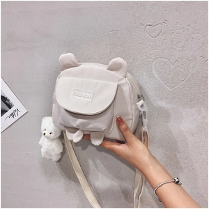 Detail of cream nylon crossbody bag with cute animal ears and plush bear charm accessory