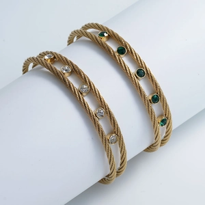 Close-up of twisted steel cable bangles with white zircon and emerald green stones