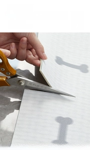 Close-up of cutting gray leather textured pet mat with bone pattern and scissors
