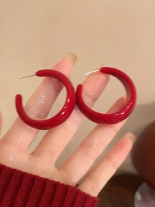 Gros plan sur les boucles d'oreilles créoles C en acrylique rouge brillant en main