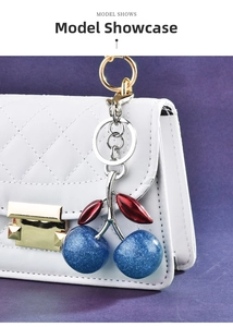Blue glitter cherry bag charm with red leaves and metal rings on a white quilted purse