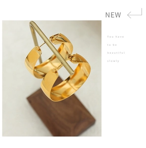 Macro detail of high-polished 18K gold-plated U-shaped thick hoop earrings on a stand