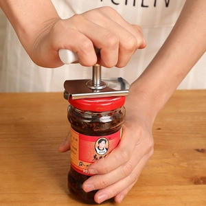 Adjustable stainless steel jar opener with white handle opening a jar on wooden table