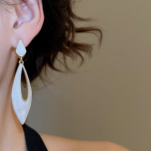 Close-up of elegant teardrop earrings with pearlescent white inlay and golden metal edges