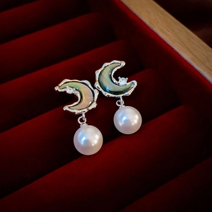 Macro view of moon-shaped pearl earrings with zircon inlay on deep red velvet