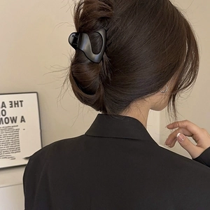 Back view of a large matte black hair claw clip securing a full bun on a woman head