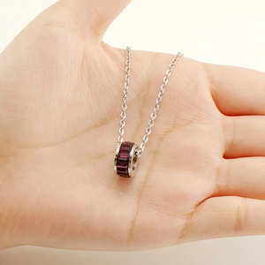 Macro shot of a silver steel necklace featuring a dark red square gemstone pendant
