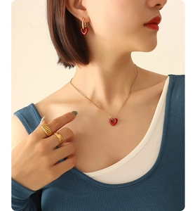 Model wearing a gold jewelry set with red heart pendants, earrings, and rings