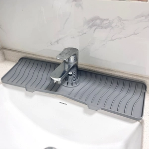 Close-up of grey silicone faucet draining mat with wavy texture on a white ceramic sink