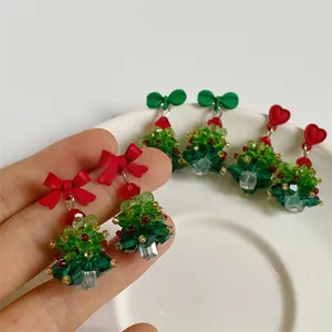 Macro shot of handmade beaded 3D Christmas tree earrings with red bows and crystals