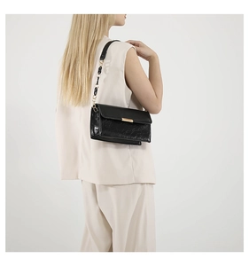 Détail du sac à bandoulière en cuir noir avec boucle dorée et chaîne sur modèle