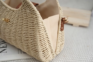 Detail of hand-woven straw beach bag with brown leather trim and golden metal lock