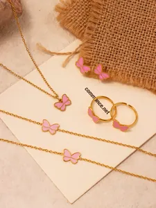 Detail view of 18k gold plated butterfly jewelry set with pink enamel on linen background