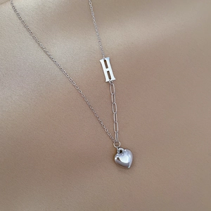 Macro detail of silver titanium steel necklace featuring letter H and heart pendant