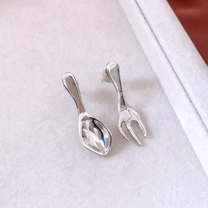 Detailed close-up of unique silver spoon and fork mismatched earrings on a beige display pad