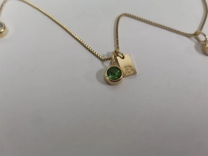 Gros plan d'un collier en maille vénitienne dorée avec gemme verte et pendentif B