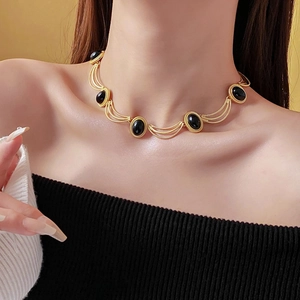 Close-up of vintage gold necklace with black oval stones worn on a model's neck