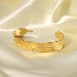 Detailed view of gold feather cuff bracelet with intricate vein texture on silk