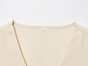 Detalle del cuello en V y la etiqueta de talla S de un conjunto beige sin mangas para mujer
