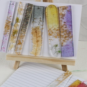 Detail of handmade resin bookmarks with dried flowers and gold foil on a notebook