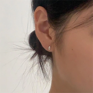 Minimalist silver teardrop stud earring shown on model ear with natural lighting detail