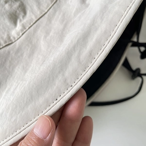 Detail of beige nylon bucket hat showing fine stitching and soft foldable fabric texture