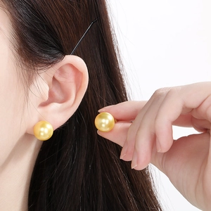 Close-up of premium golden 12mm round pearl earrings on ear with high mirror luster shine