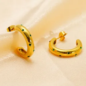 Golden C-shaped earrings with green zircon stones on champagne silk fabric background