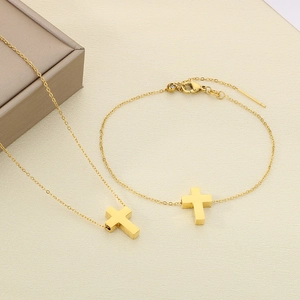 Detail of gold cross necklace and bracelet set on a textured beige surface background