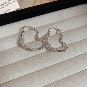 Close-up of heart-shaped twisted silver earrings presented in a beige jewelry box