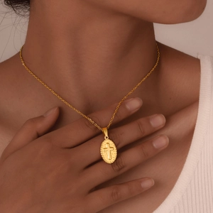 Detail of a vintage oval cross pendant necklace in gold finish on a female model