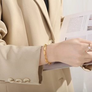 Detail of gold chain bracelet and gemstone ring worn by model in elegant beige suit