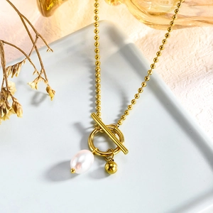Detailed shot of 18k gold plated OT clasp necklace with pearl and gold bead on ceramic tray