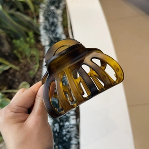 Close-up of translucent amber resin shark hair claw clip held by hand in indoor setting