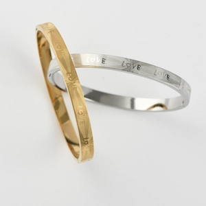 Detail of titanium steel bangle with LOVE engraving and sunburst texture in gold and silver