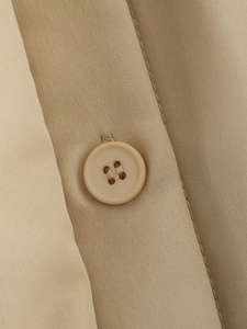 Detailed close-up of beige twill fabric and matching round four-hole button on the jacket