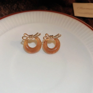 Detail of vintage bow earrings with amber resin hoop and gold-tone finish on ceramic