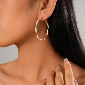 Détail d'une boucle d'oreille créole torsadée dorée à texture martelée sur un mannequin