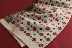 Close-up of knit winter scarf featuring festive red and black snowflake patterns