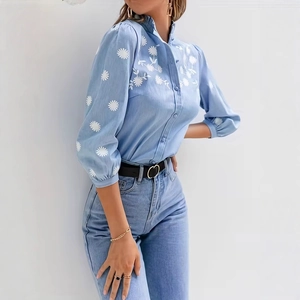 Dettaglio di ricamo a margherita bianca su camicia azzurra con maniche a sbuffo