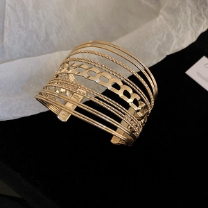 Macro detail of gold-tone multi-layer open cuff bracelet featuring hollow Cuban link style