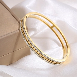 Close-up of gold stainless steel wave bracelet with sparkling crystals on white silk