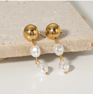 Close-up of golden stainless steel earrings with elegant dangling baroque pearls on stone